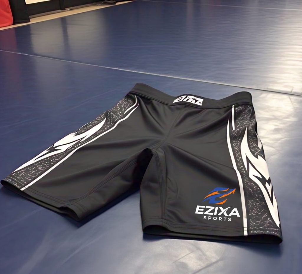 Angled view of black EZIXA Sports MMA fight shorts with textured tribal side panels resting on a gym mat.